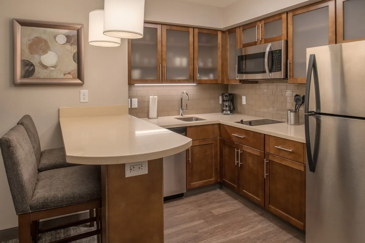 This image shows a cozy and inviting kitchen area featuring a spacious countertop with stools, modern appliances including a stove and microwave, and well-organized cabinetry. The scene suggests activity, such as preparing meals or sharing breakfast, and the overall setting feels homey yet upscale.