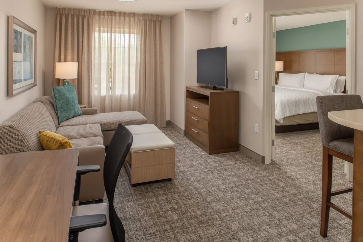 The image showcases a stylish, comfortable interior with a plush sofa facing a large television, a dining table perfect for shared meals, and an inviting entrance to the bedroom. The room feels bright and welcoming, ideal for both relaxation and productivity.