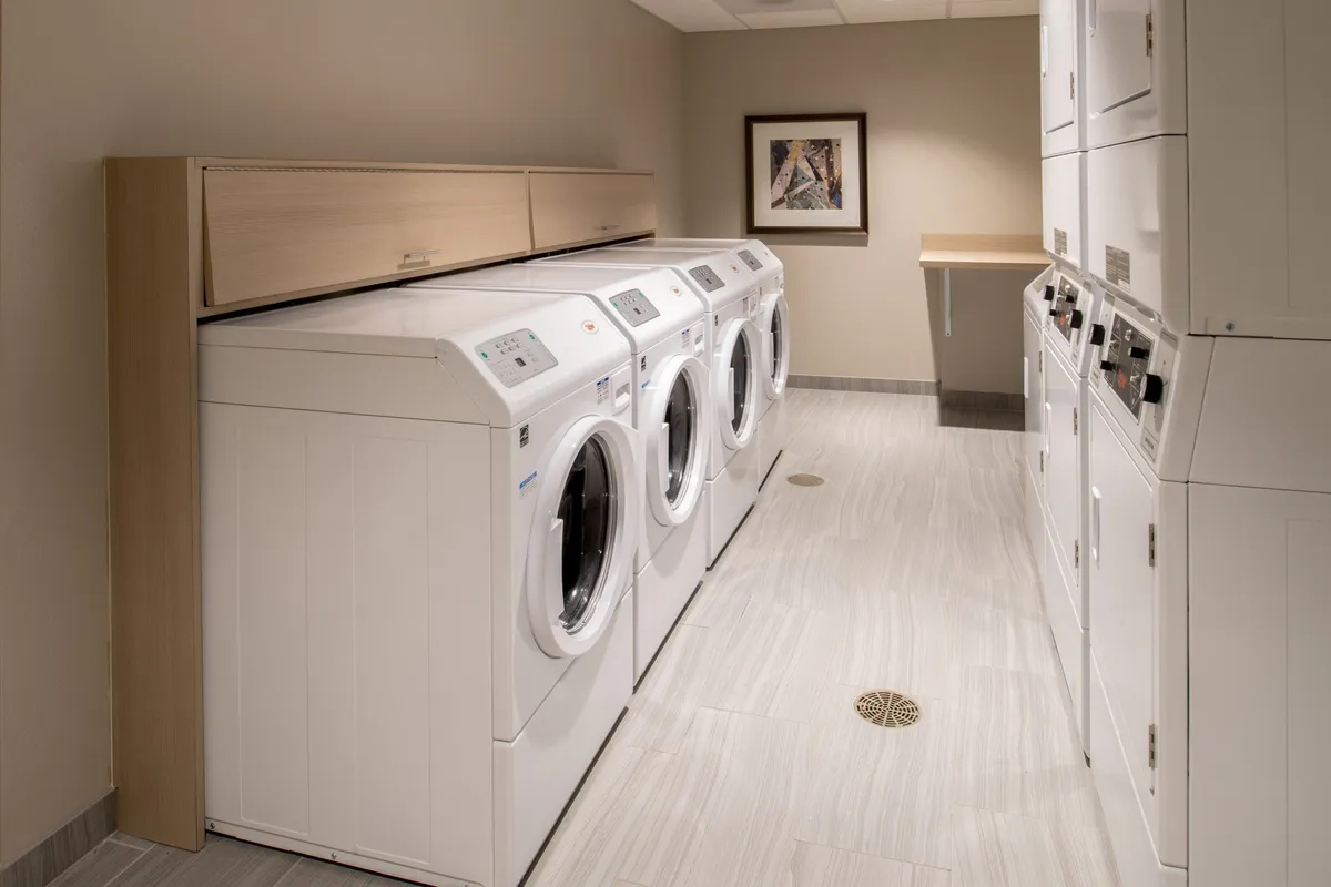 A practical laundry area featuring multiple washing machines, dryers, ample counter space for folding, and framed artwork to add a welcoming touch. The environment is clean, organized, and designed for efficient use by guests.